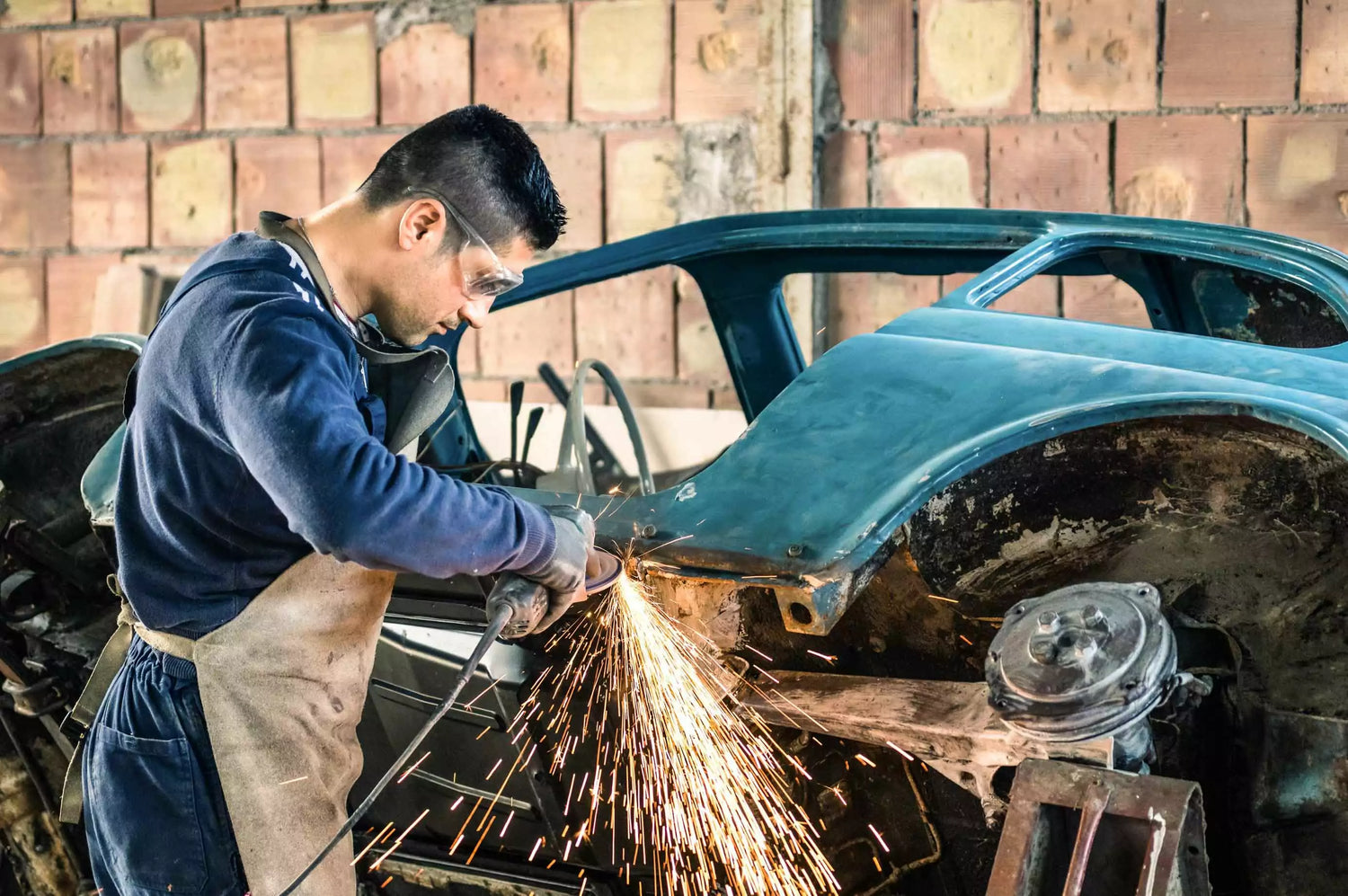 A man is tinkering with a car while an industrial air cleaner filters the air in the garage.