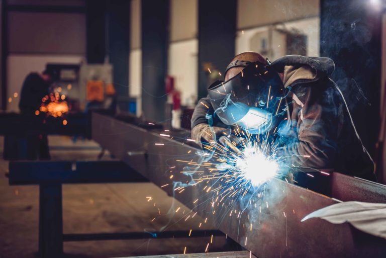 A welder is using an industrial air cleaner to ensure clean air while welding metal in a factory.