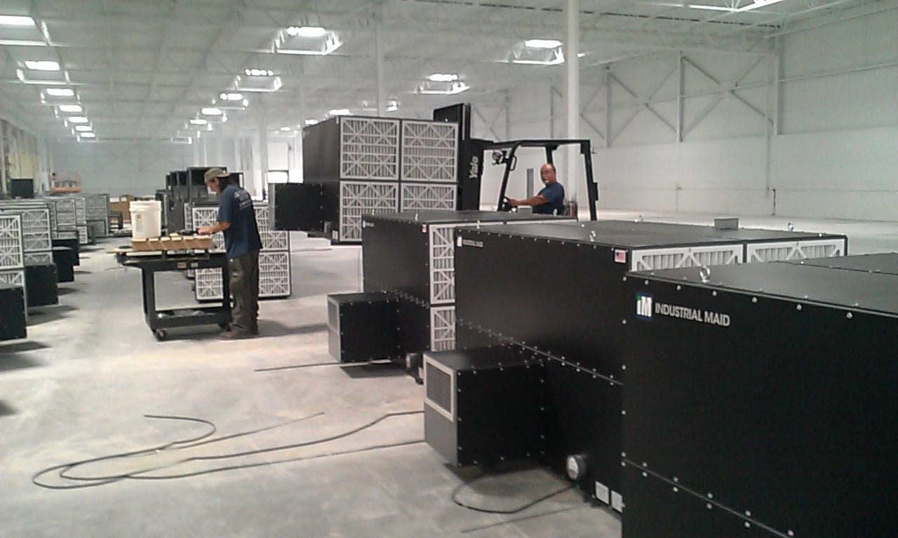Men in a warehouse with large machines work in a clean shop air environment thanks to an air cleaner.