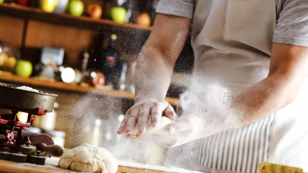 A man is kneading dough in a kitchen while using an industrial air cleaner.