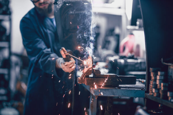 A man welding a piece of metal using an industrial air cleaner.