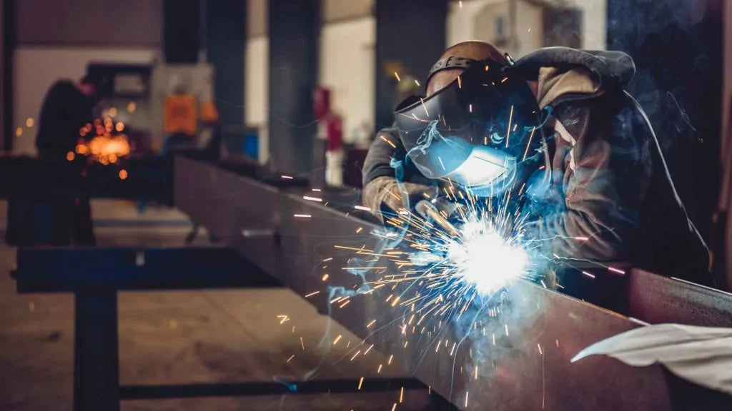 A man welding a metal piece in a clean shop air environment.